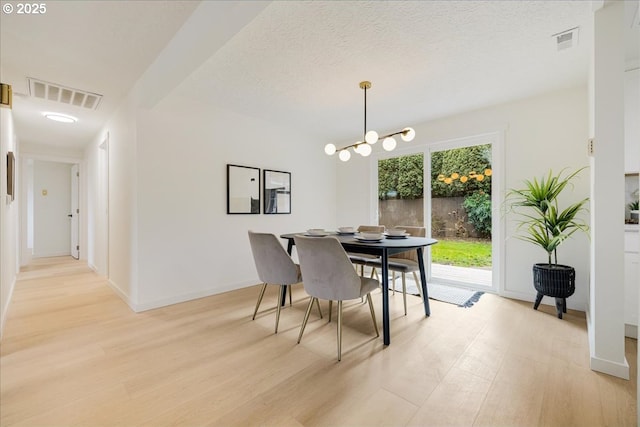 dining area featuring an inviting chandelier, light hardwood / wood-style floors, and a textured ceiling