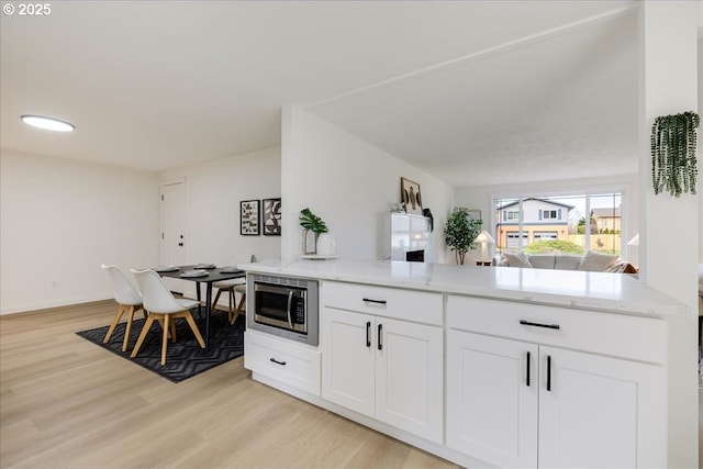 kitchen with stainless steel microwave, white cabinets, light wood-type flooring, and light stone counters