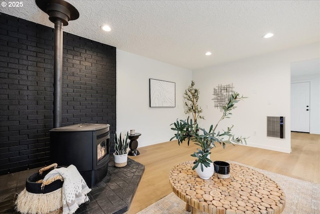 living room with hardwood / wood-style floors, brick wall, a textured ceiling, and a wood stove