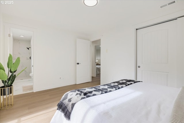 bedroom featuring a closet, ensuite bathroom, and light hardwood / wood-style flooring