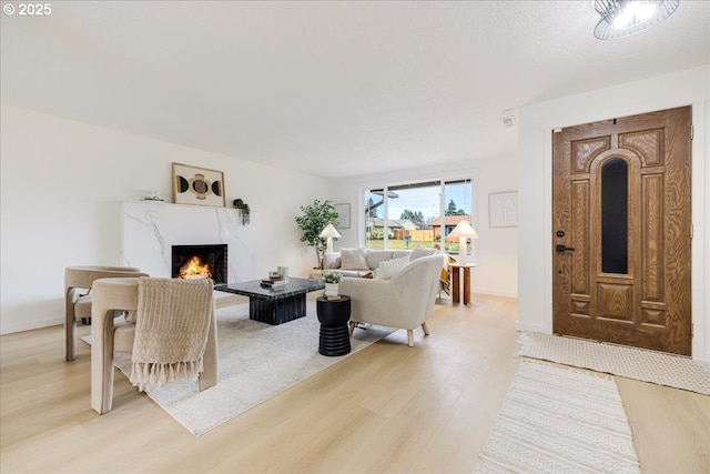 living room with a high end fireplace, a textured ceiling, and light wood-type flooring