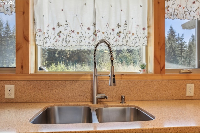 kitchen view of a sink, backsplash, and light stone countertops