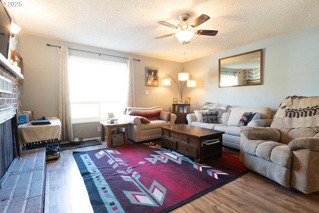 living room with a textured ceiling, ceiling fan, a fireplace, and wood finished floors