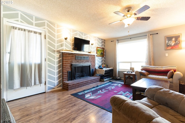 living area with ceiling fan, a textured ceiling, a fireplace, and wood finished floors