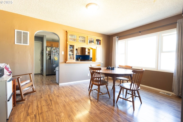 dining room with arched walkways, a textured ceiling, visible vents, baseboards, and light wood-style floors