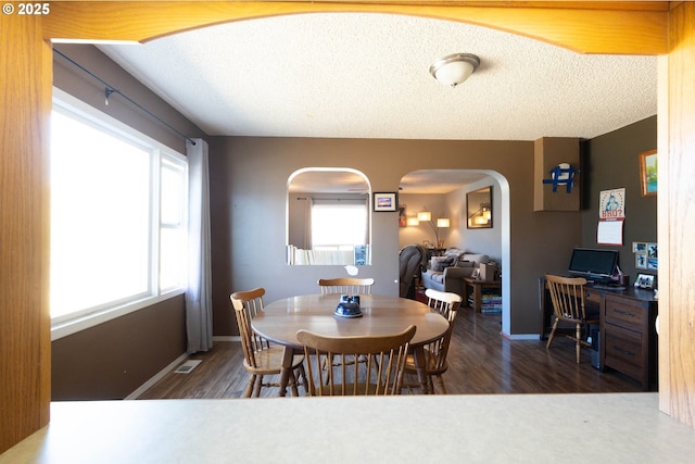 dining area with arched walkways, a healthy amount of sunlight, a textured ceiling, and wood finished floors