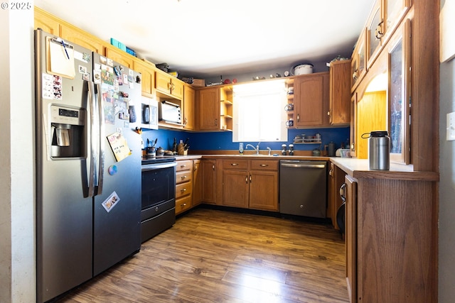 kitchen with brown cabinetry, dark wood finished floors, stainless steel appliances, open shelves, and a sink