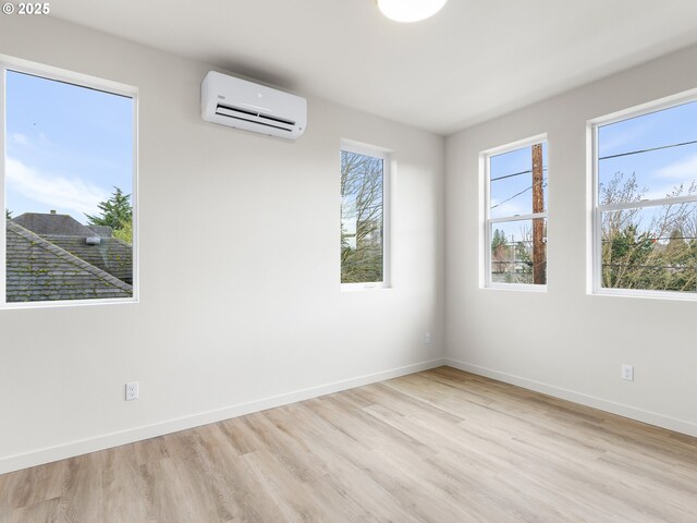 spare room with light wood-type flooring, baseboards, and a wall mounted AC