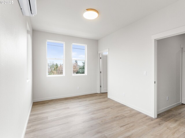 spare room with light wood-style flooring, an AC wall unit, and baseboards