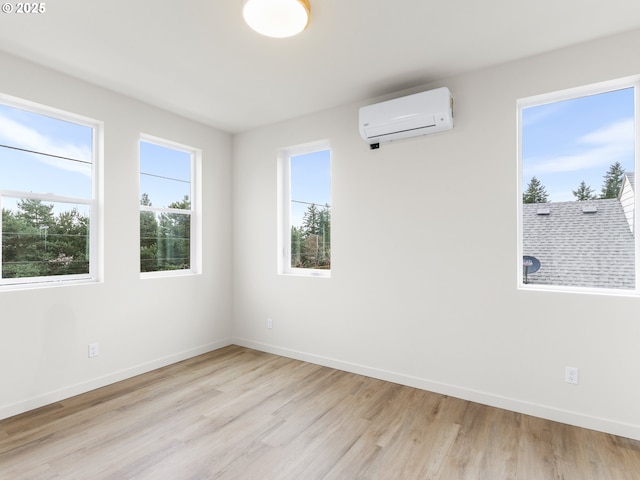 unfurnished room with light wood finished floors, a wall mounted AC, and baseboards