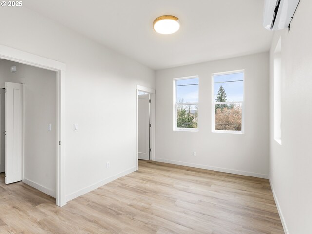 unfurnished room with light wood-type flooring, baseboards, and a wall unit AC