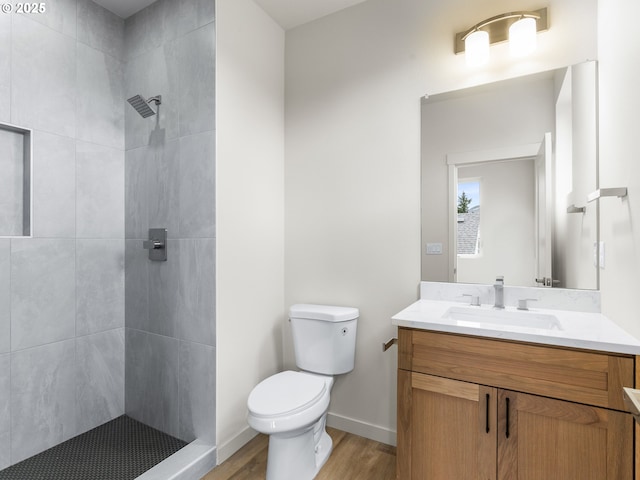 bathroom featuring vanity, toilet, wood finished floors, and tiled shower
