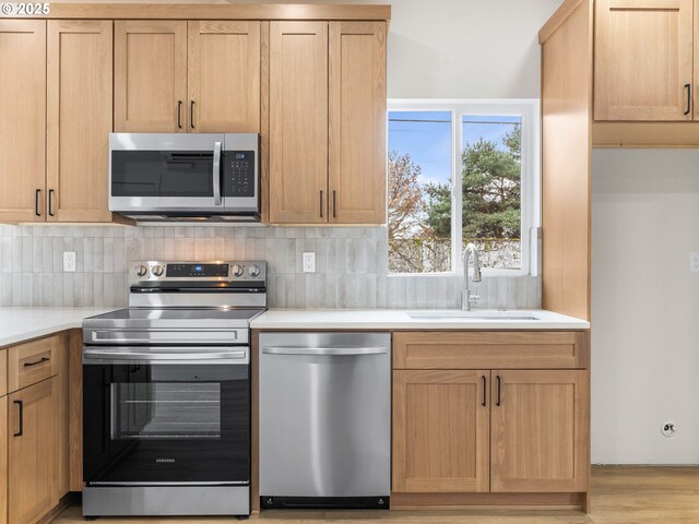 kitchen featuring light wood-style flooring, a sink, tasteful backsplash, appliances with stainless steel finishes, and light countertops