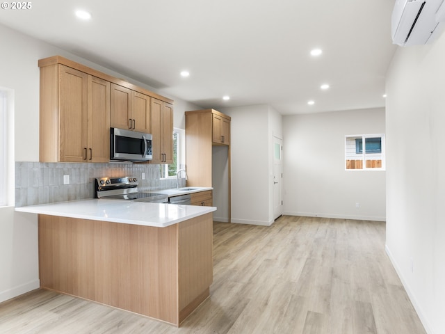 kitchen with a wall mounted AC, backsplash, appliances with stainless steel finishes, a peninsula, and light countertops