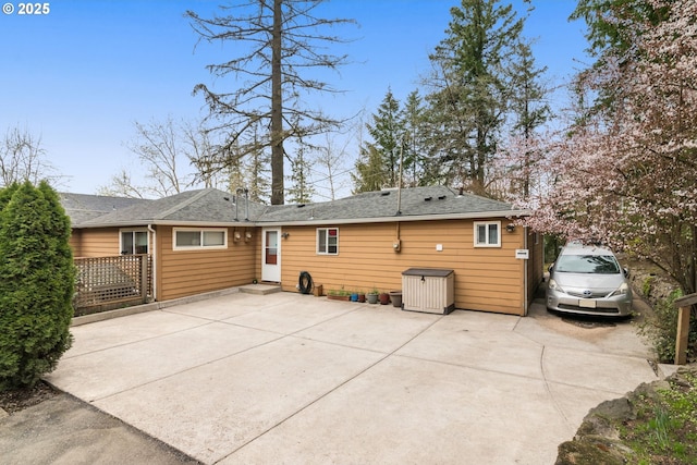 back of house with driveway, roof with shingles, and a patio area