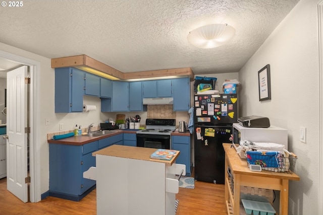 kitchen featuring blue cabinetry, under cabinet range hood, freestanding refrigerator, and range with electric stovetop