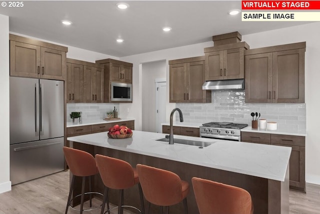 kitchen with sink, light wood-type flooring, an island with sink, and appliances with stainless steel finishes