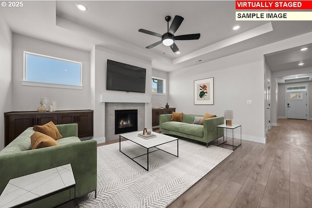 living room featuring ceiling fan, light wood-type flooring, and a tray ceiling