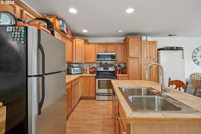 12631 SE Division St, Portland, OR 97236 - kitchen with visible vents, a sink, appliances with stainless steel finishes, light wood-style floors, and tile counters