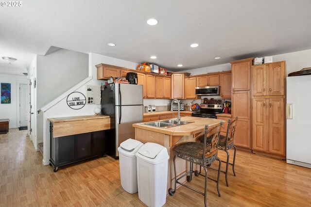 12631 SE Division St, Portland, OR 97236 - kitchen featuring a sink, light wood-type flooring, appliances with stainless steel finishes, a kitchen island with sink, and a breakfast bar area