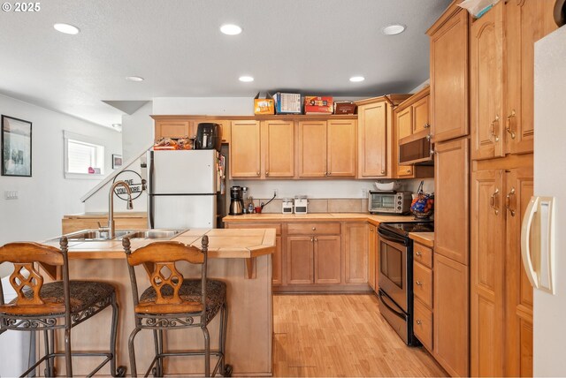 12631 SE Division St, Portland, OR 97236 - kitchen with recessed lighting, light wood-style flooring, a kitchen bar, appliances with stainless steel finishes, and a sink