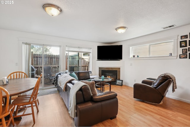 12631 SE Division St, Portland, OR 97236 - living area with a glass covered fireplace, visible vents, light wood-type flooring, and a textured ceiling