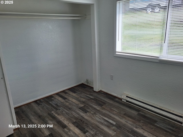unfurnished bedroom with baseboards, baseboard heating, dark wood finished floors, and a textured wall