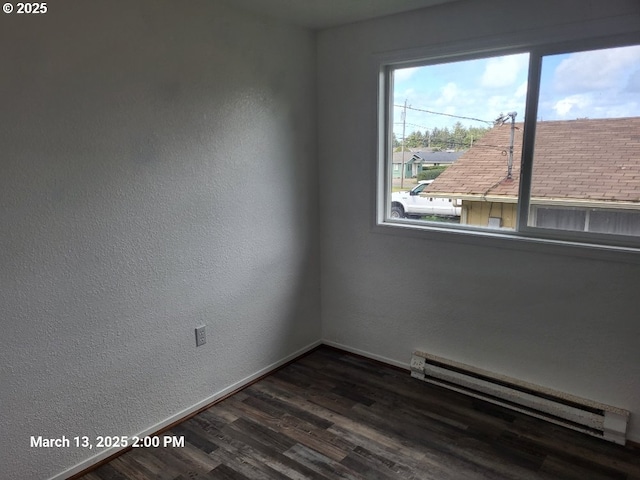 spare room with a baseboard heating unit, dark wood-type flooring, a textured wall, and baseboards