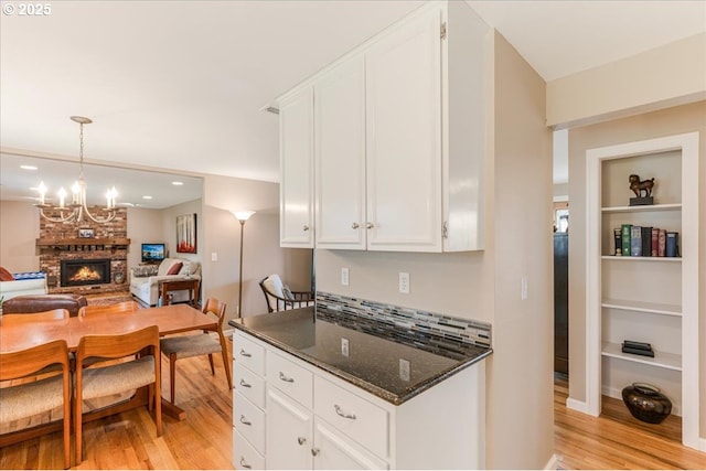 kitchen featuring dark stone counters, a stone fireplace, white cabinets, and light wood finished floors