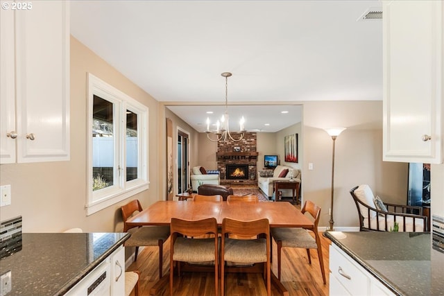 dining room featuring wood finished floors, baseboards, visible vents, an inviting chandelier, and a fireplace