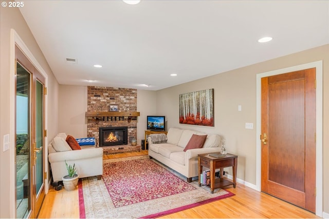 living area with visible vents, baseboards, recessed lighting, light wood-style floors, and a brick fireplace