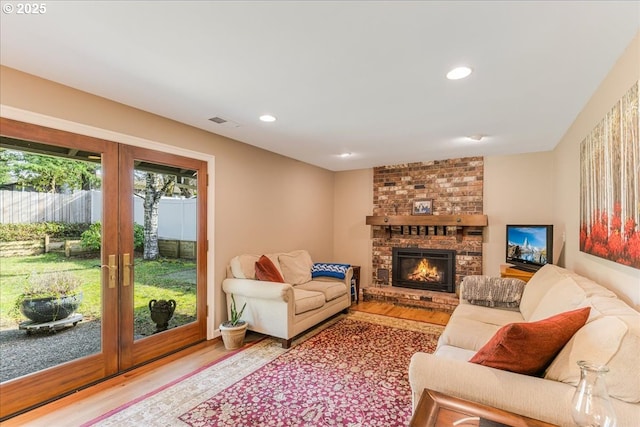 living room with wood finished floors, visible vents, recessed lighting, french doors, and a brick fireplace