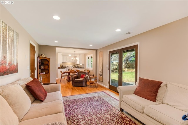 living room with visible vents, light wood-type flooring, recessed lighting, french doors, and a notable chandelier