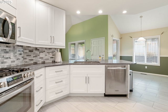 kitchen with dark stone counters, a sink, vaulted ceiling, white cabinets, and appliances with stainless steel finishes