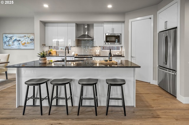 kitchen featuring wall chimney range hood, modern cabinets, a sink, a breakfast bar, and stainless steel appliances