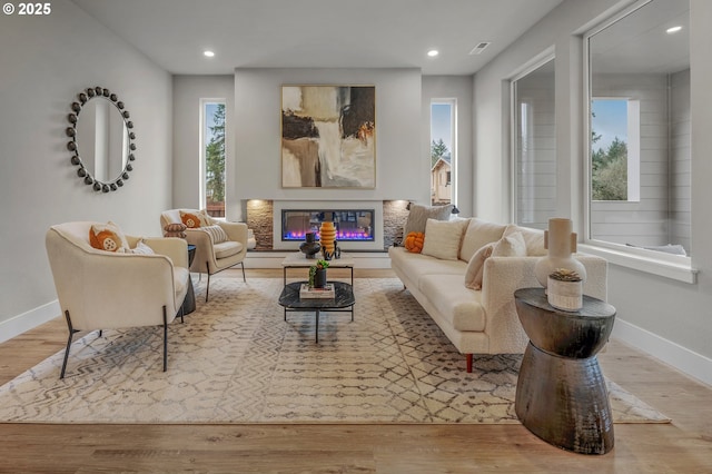 living area with a glass covered fireplace, baseboards, wood finished floors, and a wealth of natural light