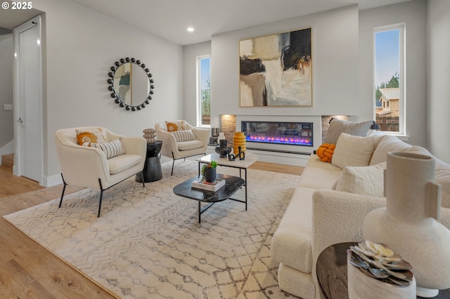 living area with recessed lighting, baseboards, a glass covered fireplace, and wood finished floors