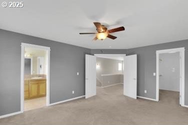 unfurnished bedroom with ceiling fan, ensuite bathroom, a walk in closet, and light carpet