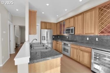 kitchen with appliances with stainless steel finishes, sink, tasteful backsplash, a center island with sink, and beverage cooler