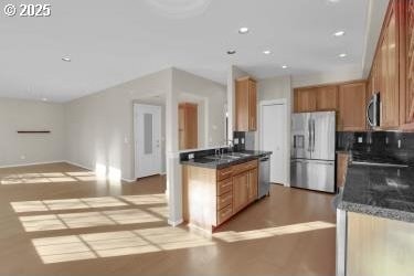 kitchen featuring appliances with stainless steel finishes, tasteful backsplash, sink, light hardwood / wood-style flooring, and dark stone counters