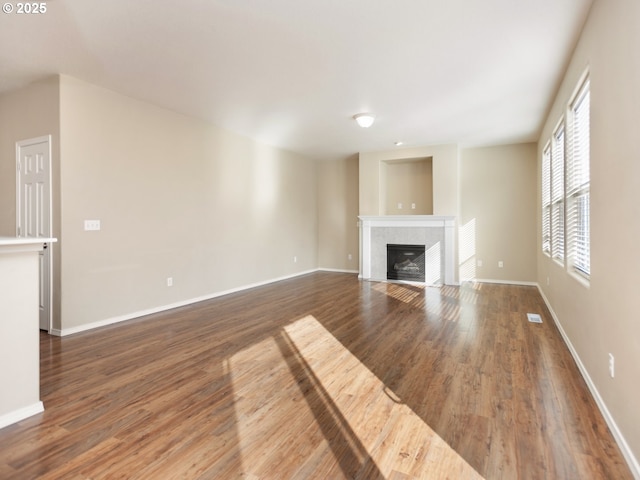 unfurnished living room with visible vents, a fireplace, baseboards, and wood finished floors