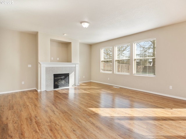 unfurnished living room featuring light wood-style flooring, visible vents, baseboards, and a tile fireplace