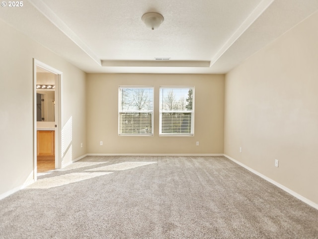 spare room with a textured ceiling, visible vents, baseboards, a tray ceiling, and carpet