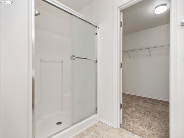 bathroom with a stall shower, a walk in closet, and baseboards