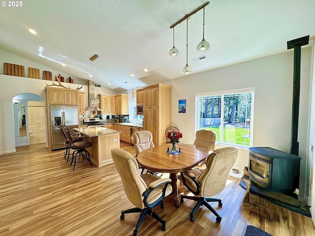 dining space featuring a wood stove, vaulted ceiling, arched walkways, light wood-style flooring, and recessed lighting