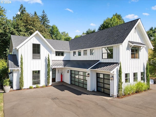 modern farmhouse style home featuring metal roof, a shingled roof, driveway, board and batten siding, and a standing seam roof