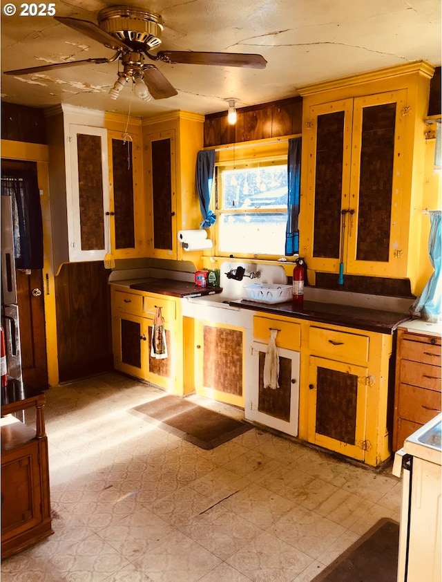 kitchen with light flooring, ceiling fan, white electric range, and wood walls