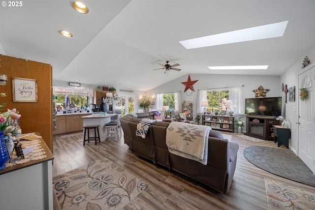 living room featuring a skylight, plenty of natural light, lofted ceiling, light wood-style flooring, and a glass covered fireplace