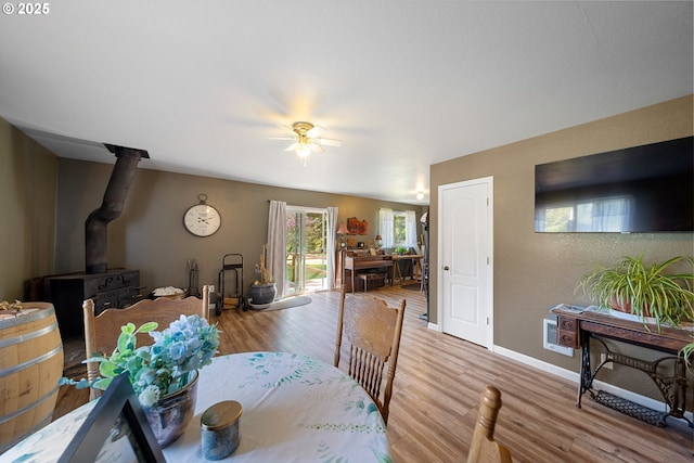 dining area with a wood stove, wood finished floors, a ceiling fan, and baseboards