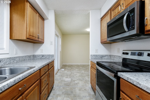 kitchen featuring brown cabinets, a textured ceiling, stainless steel appliances, light countertops, and baseboards